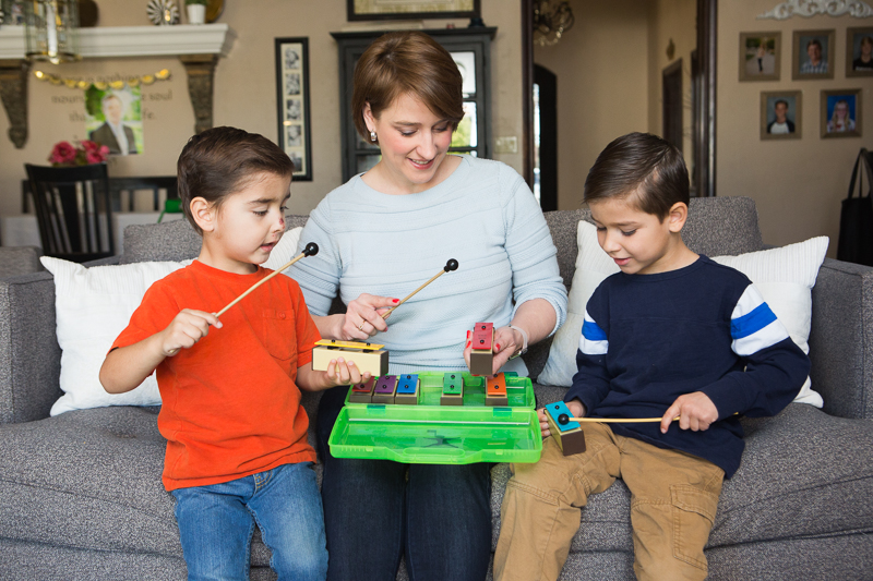 Two young kids learning to play an instrument by a woman.