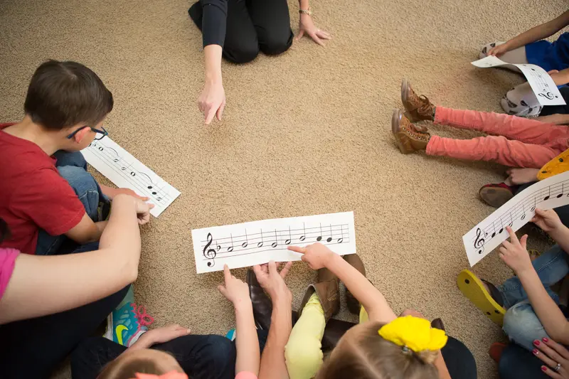 Many young kids reading music in a circle.